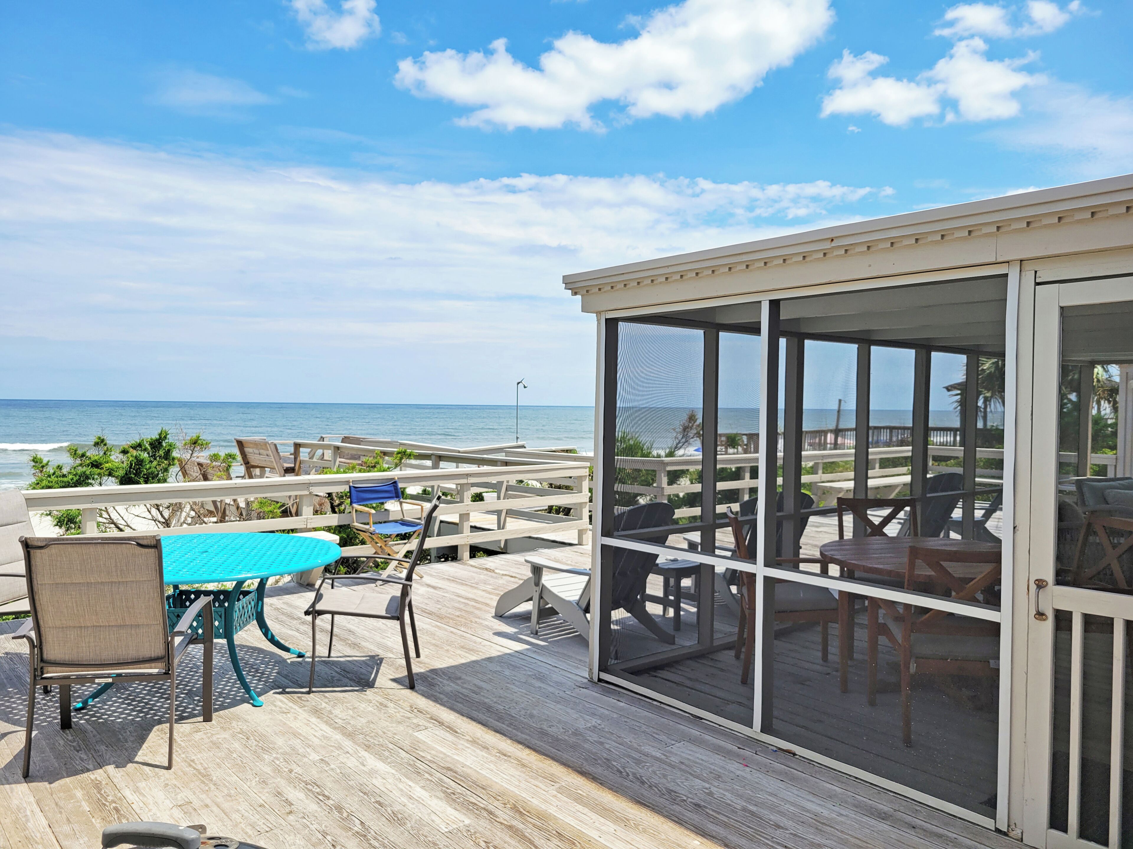 Une terrasse extérieure couverte avec vue sur l’océan, comprenant une table et des chaises, ainsi qu’un espace clos par des parois de verre avec des sièges supplémentaires.