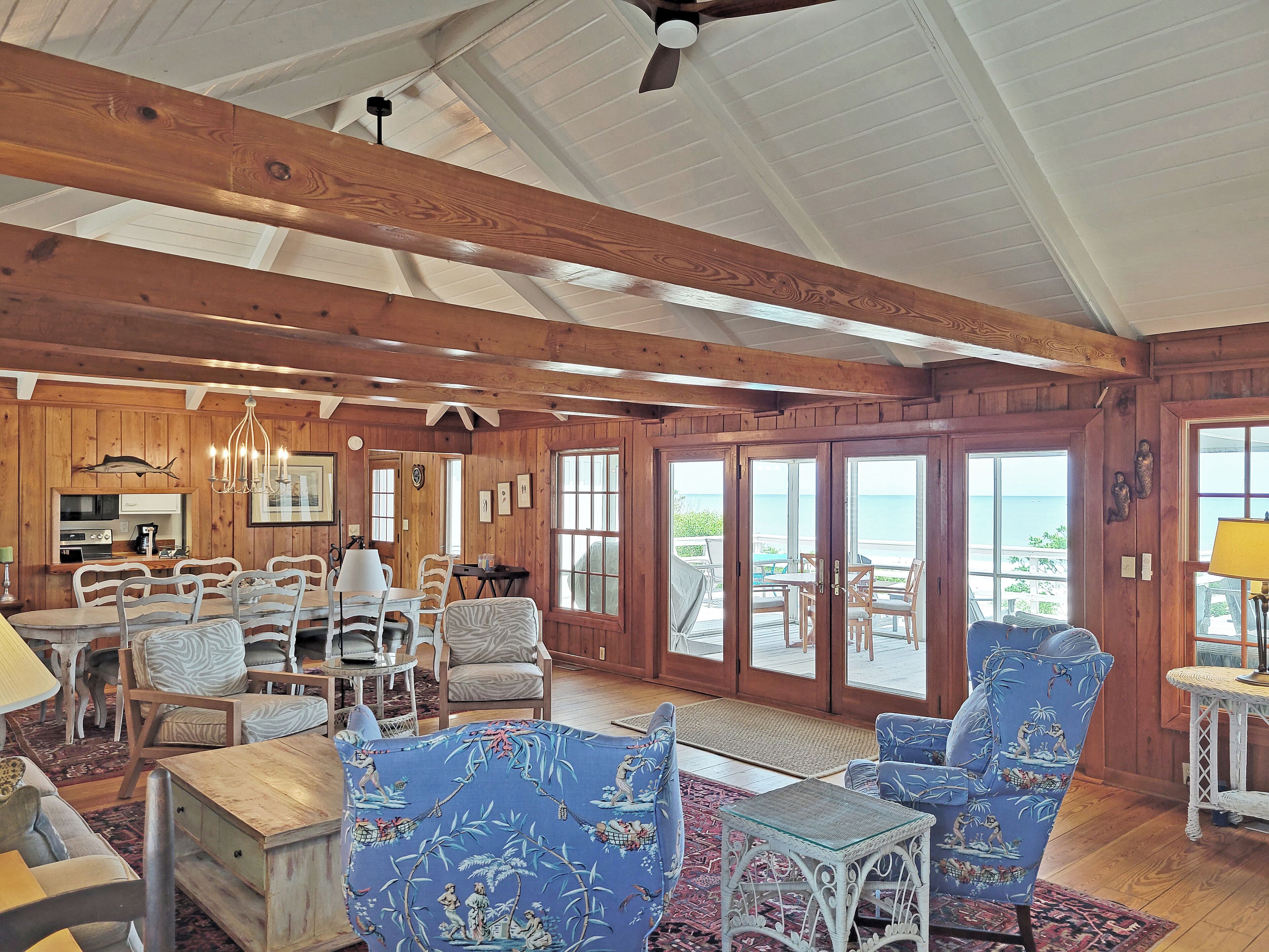 A spacious living area with wooden beams, a dining set, and a view through large sliding doors to the outside.