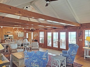 Amplia sala de estar con vigas de madera, un comedor y vistas al exterior a través de grandes puertas correderas.