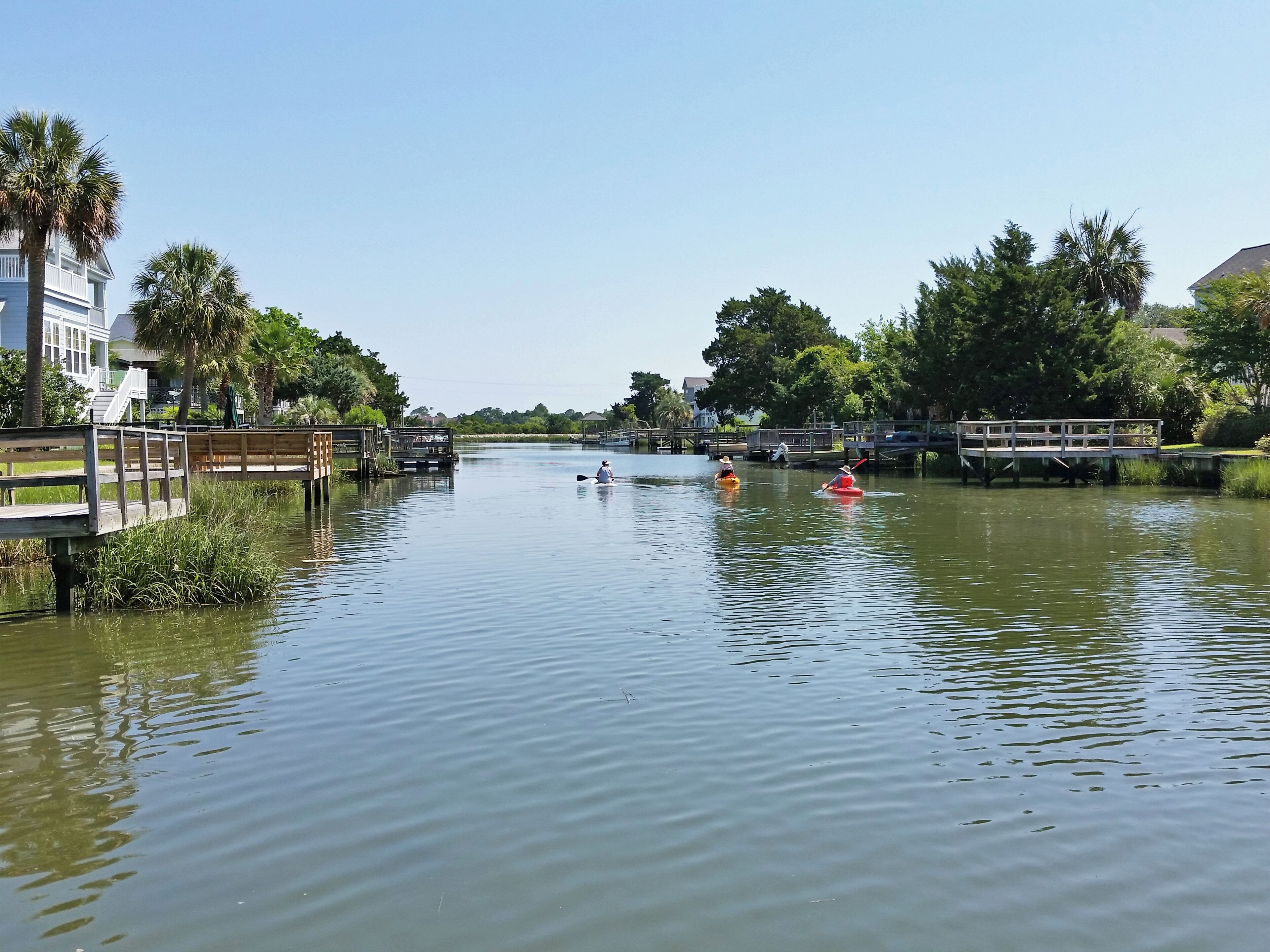 A calm river with kayaks, wooden walkways, and lush greenery.