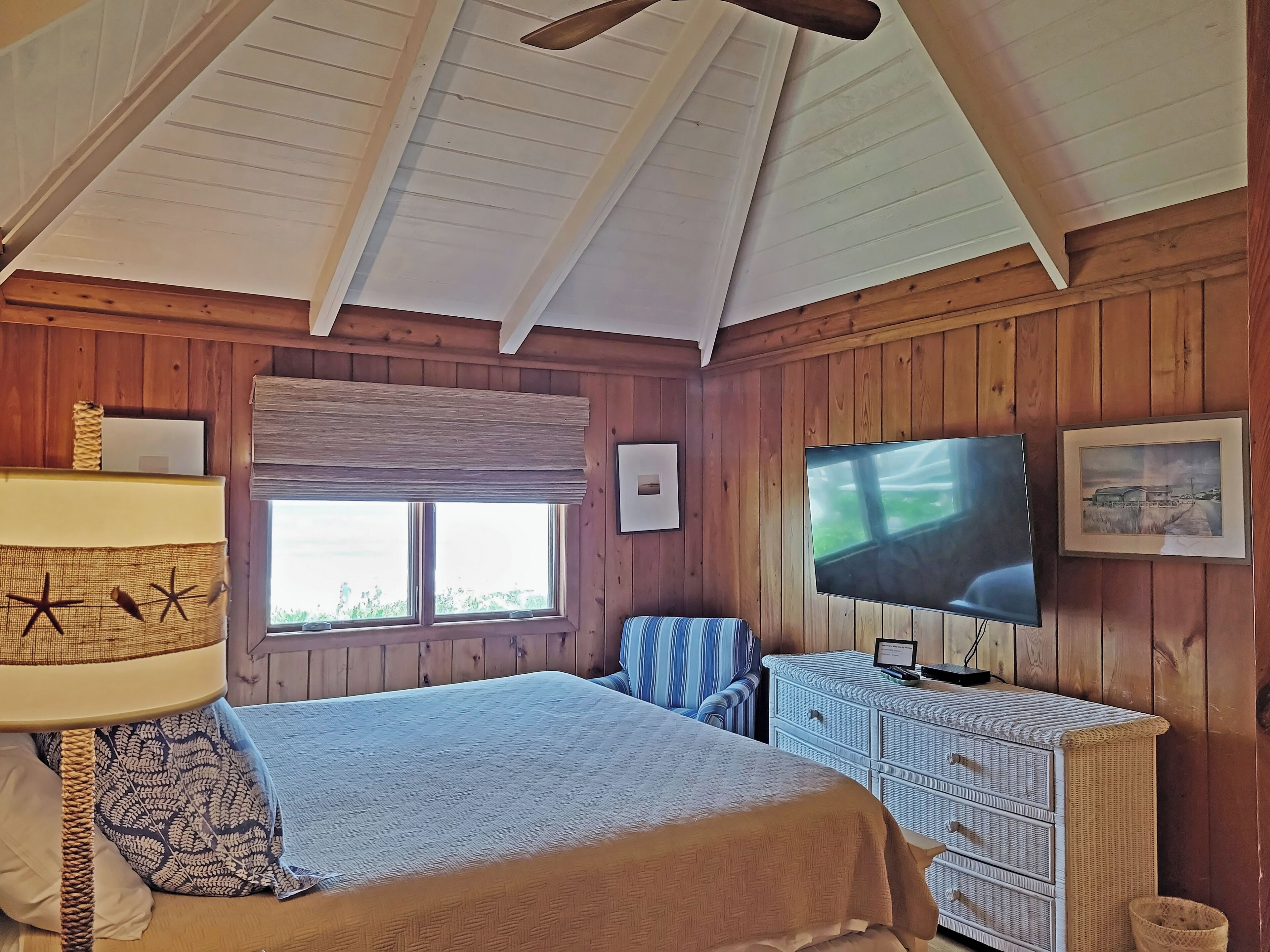 A bedroom with a bed, a TV, a window, and wooden walls.