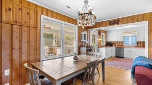 Une cuisine spacieuse avec un lambris en bois, un coin repas avec une table et des chaises en bois, et une vue sur l’extérieur grâce à de grandes fenêtres.