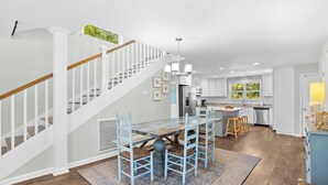 Une cuisine moderne dotée d’un îlot central, de meubles blancs et d’un escalier avec des rampes en bois.