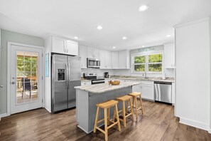 Una cocina moderna con armarios blancos, electrodomésticos de acero inoxidable y una isla grande con taburetes.