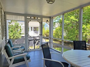 A covered porch with a table and chairs, a view of a blue house, and a white fence.