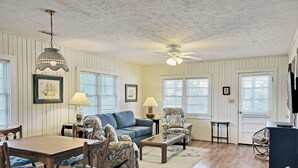 Ein gemütliches Wohnzimmer mit Holzboden, einem blauen Sofa, einem gemusterten Sessel, einem Couchtisch und einem Deckenventilator.