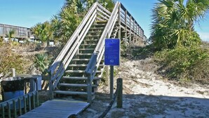 Eine Holztreppe führt zu einem Strandbereich mit einem Schild.