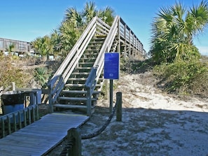 A wooden staircase leading to a beach area with a signboard.