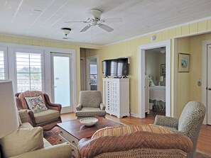 A room with a ceiling fan, a television, a cabinet, and a door leading to another room.