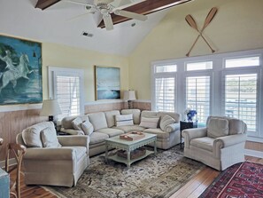 A living room with a high ceiling, a ceiling fan, a large painting, a sofa set, a coffee table, and a patterned rug.