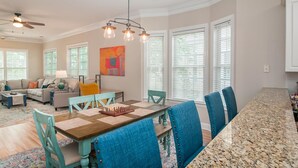 A spacious living room with a large dining table, blue upholstered chairs, and a ceiling fan.