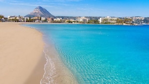 Uma praia com águas turquesa cristalinas, areia dourada e uma montanha ao fundo.