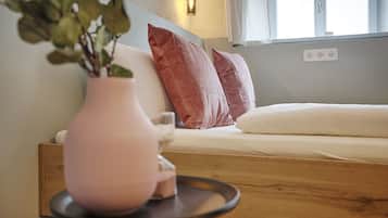 Ein gemütliches Zimmer mit einem Bett, einem Nachttisch mit einer Vase und einem Fenster mit Blick.