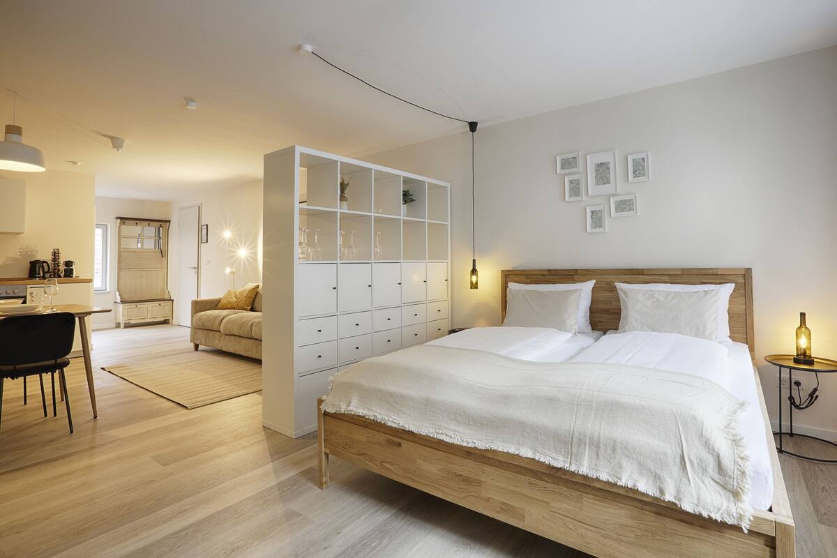 A modern bedroom with a wooden bed, a white wardrobe, and a dining area with a table and chairs.