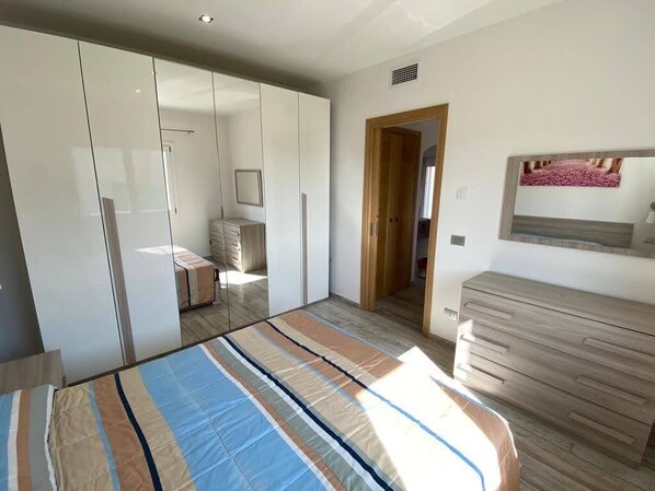 A bedroom with a bed, a wardrobe, a dresser, and a mirror on the wall.