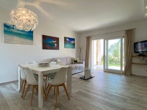 A modern living room with a dining area, large windows, and artwork on the walls.