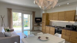 A modern kitchen with wooden cabinets, a dining area with a white table and chairs, and a TV on the wall. - R House 2 independent semi-detached house (Budoni)