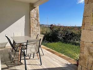 A patio with a table and chairs, stone walls, and a view of a green landscape.