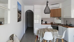 A compact kitchen with white cabinets, a dining area with a table and chairs, and a hanging pendant light.