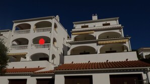 A multi-story building with balconies, a red roof, and a white facade.