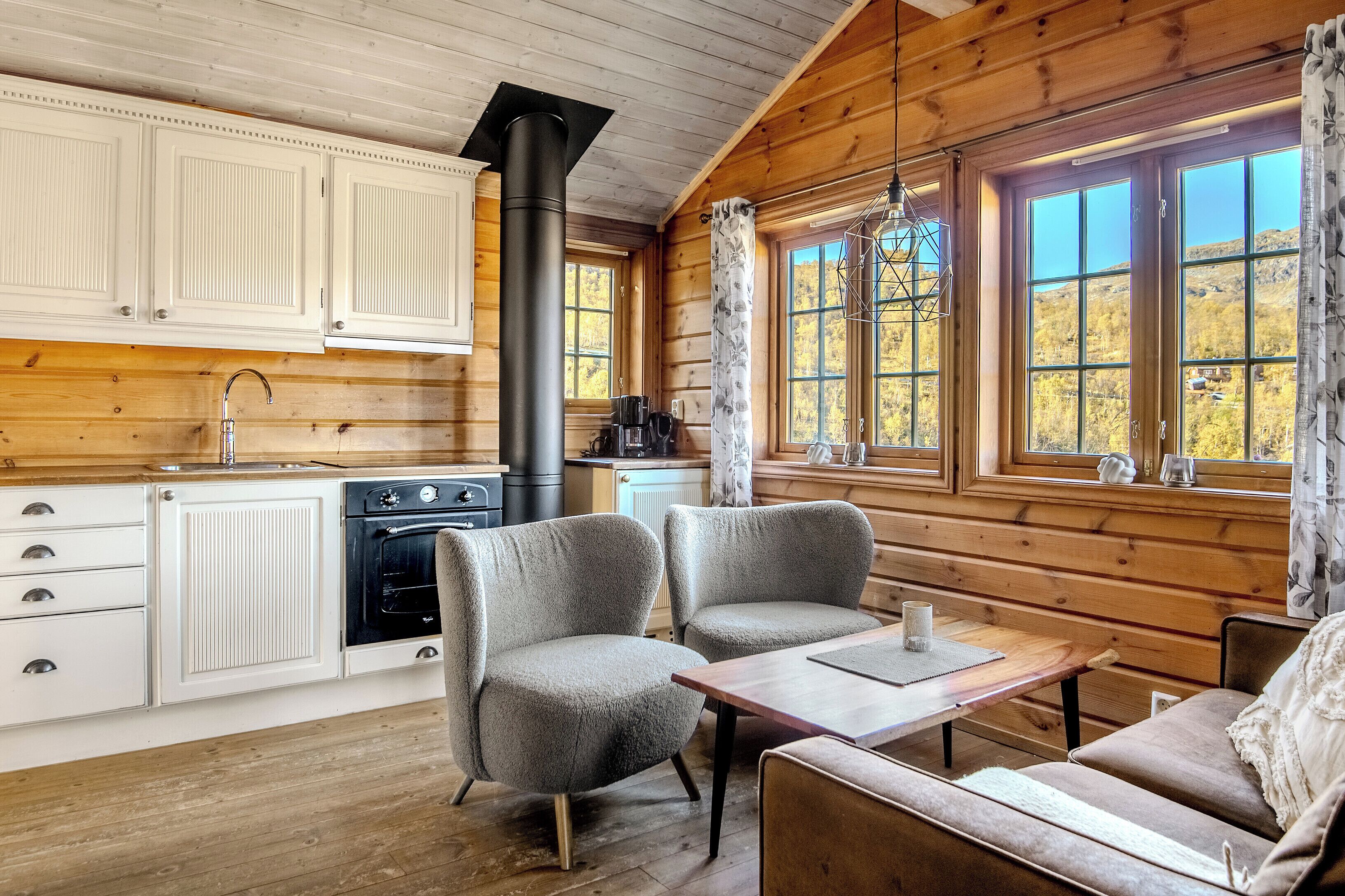 A wooden cabin interior with a kitchen, dining area, and large windows.