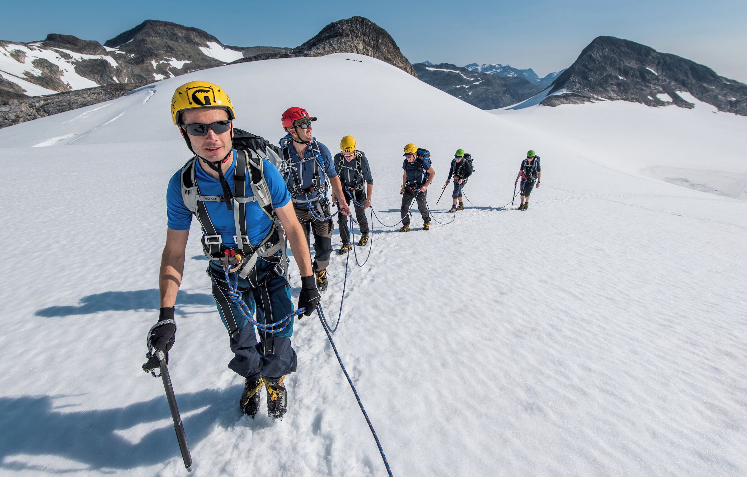 Un grupo de personas en un sendero nevado de montaña, con cielo despejado y montañas a lo lejos.