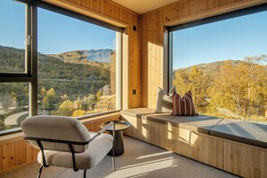 A room with large windows, a cushioned bench, a chair, and a small table.