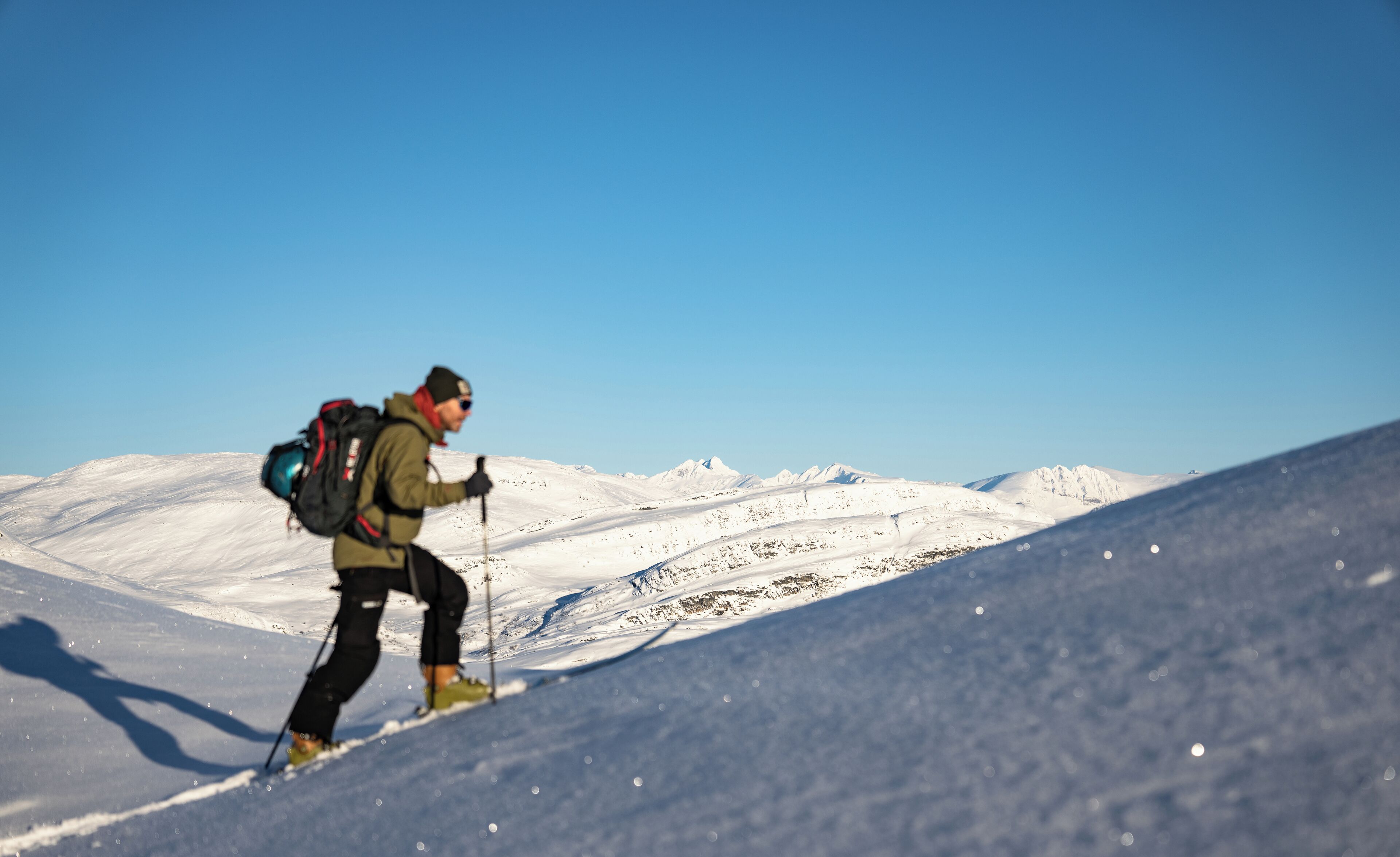 A person hiking on a snow-covered slope with a clear sky.