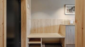 A wooden bench with a low backrest and a small shelf underneath, positioned against a wall with a light-colored panel.