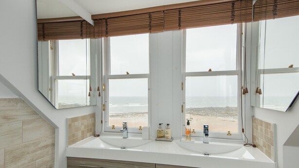 A bathroom with two sinks, a mirror, and a view of the beach. - A 4-bedroom luxury holiday home with enchanting sea views across Milsey Bay Beach (North Berwick)