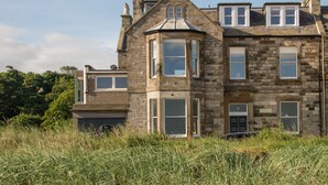 A stone building with multiple windows and a bay window, surrounded by tall grass. - A 4-bedroom luxury holiday home with enchanting sea views across Milsey Bay Beach (North Berwick)