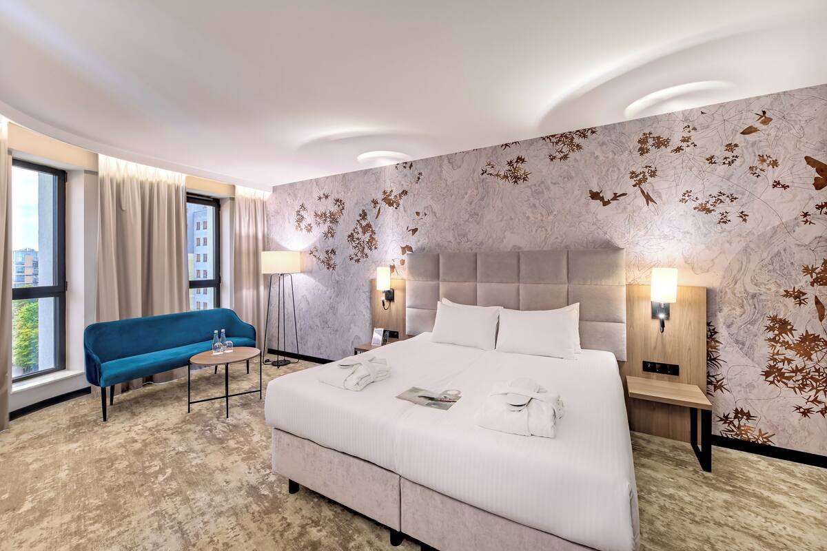 A hotel room with a large bed, a blue sofa, a small table, and a window with curtains.