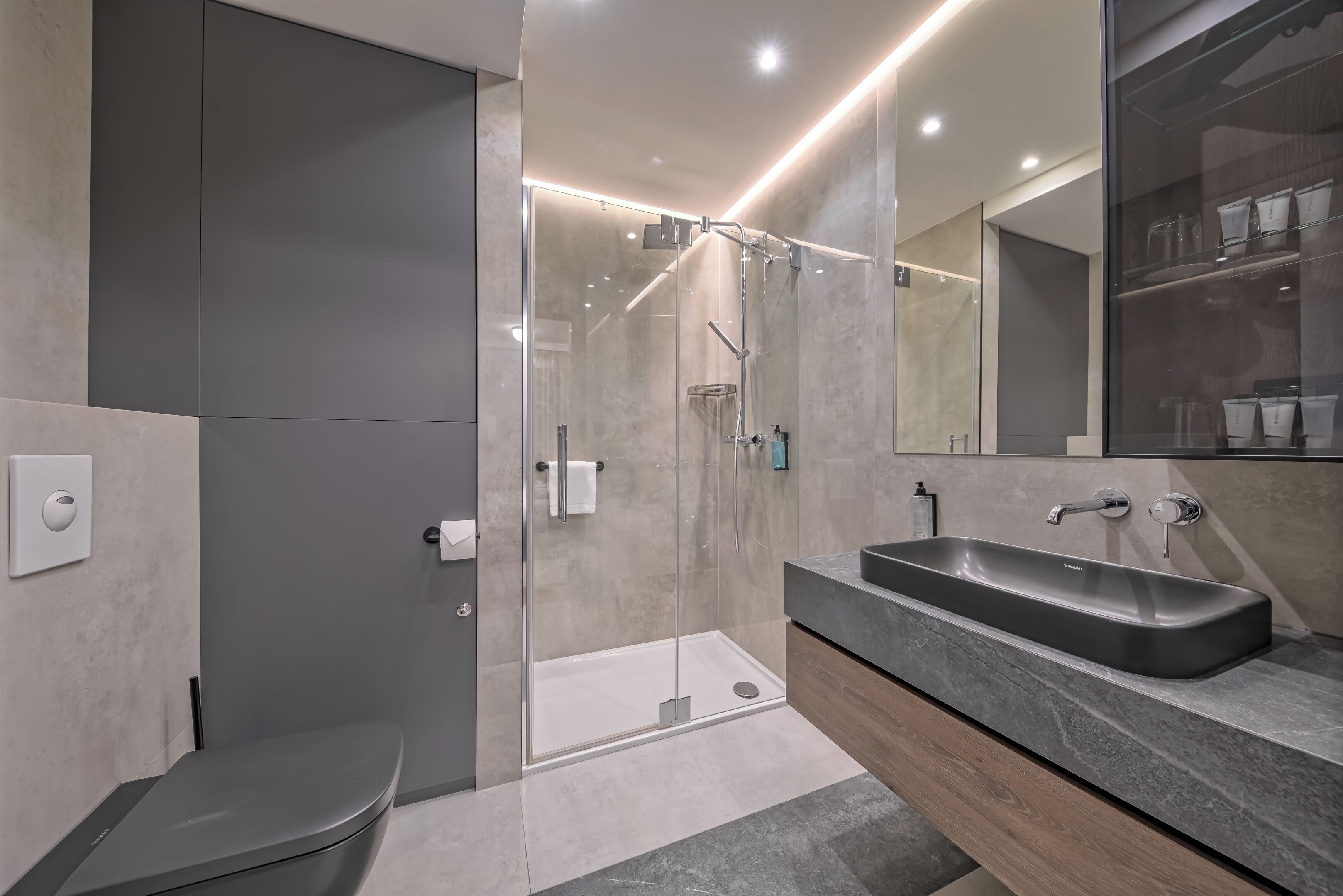 Un baño moderno con ducha de vidrio, tocador con lavamanos y un inodoro.