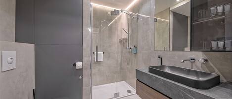 Un baño moderno con ducha de vidrio, tocador con lavamanos y un inodoro.