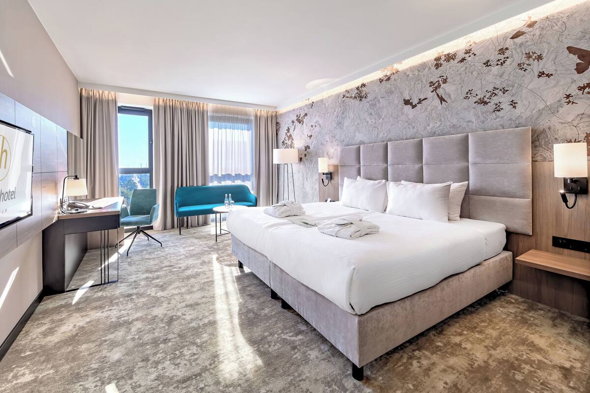 A hotel room with a large bed, a desk, a blue sofa, and a view of the city.