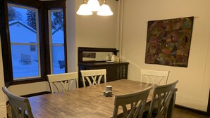 A dining room with a wooden table and chairs, a kitchen area with cabinets and a countertop, and a window with a view of a snowy landscape. - Stately home in Washburn  (Washburn)