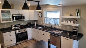 A modern kitchen with white cabinets, a stainless steel range, a microwave, and a dishwasher. There is a window with a view of trees and a clock on the wall. - Stately home in Washburn  (Washburn)
