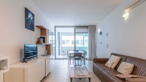Een moderne woonkamer met een flatscreen televisie, een eettafel met stoelen, een bruine leren bank en een grote schuifglazen deur die leidt naar een balkon.