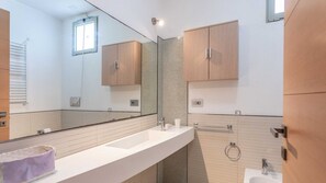 Een moderne badkamer met een grote spiegel, houten kastjes, een witte wasbak en een handdoekrek.
