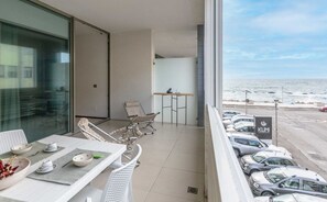 Een balkon met een gedekte eettafel, een stoel en uitzicht op de oceaan en geparkeerde auto's.