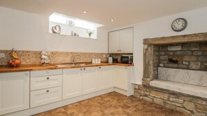 A modern kitchen with white cabinets, a stone fireplace, a microwave, and a clock on the wall. - 1 The Riverside (Barnard Castle)