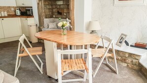 A cozy dining area with a round wooden table and white chairs, a vase of flowers, and a stone fireplace in the background. - 1 The Riverside (Barnard Castle)
