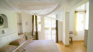 Ein Schlafzimmer mit einem Bett, einem Nachttisch, einem Stuhl, einem Fenster mit Vorhang und einer Kommode.