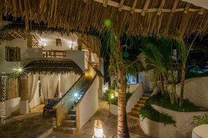 A staircase leading to a terrace with a thatched roof, surrounded by greenery and a white wall. - Zawadi Residence (Watamu)