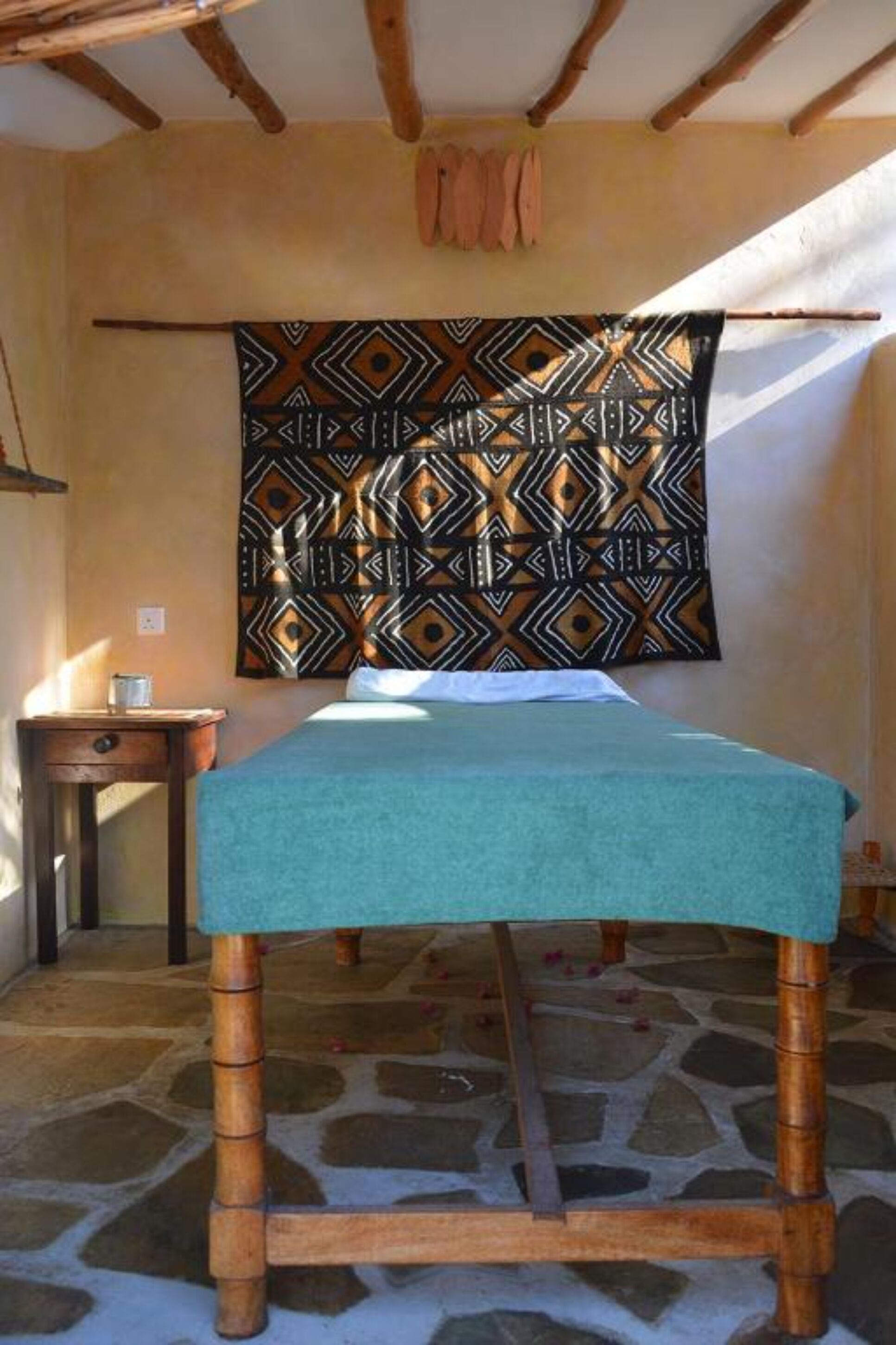 A room with a bed, a wooden nightstand, a patterned tapestry, and a stone floor.