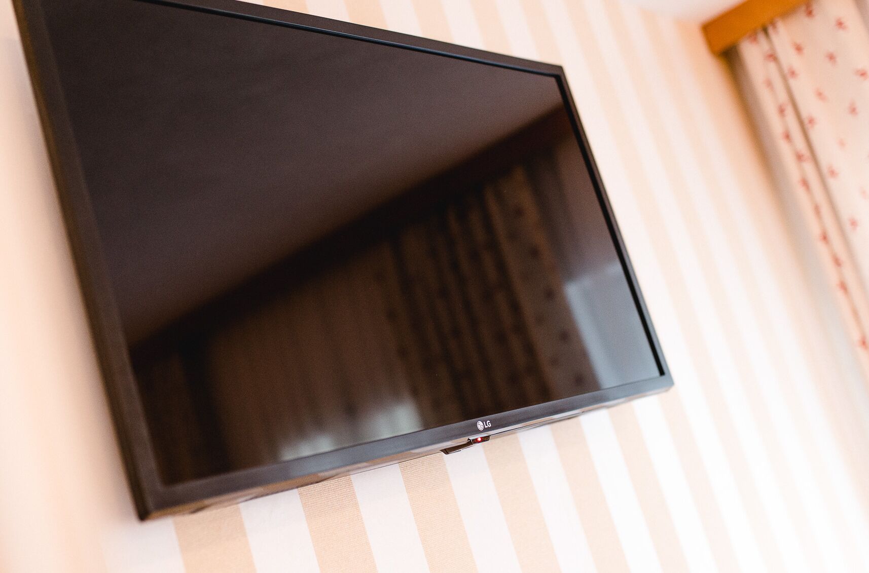 A flat-screen TV mounted on a wall with a striped wallpaper background.