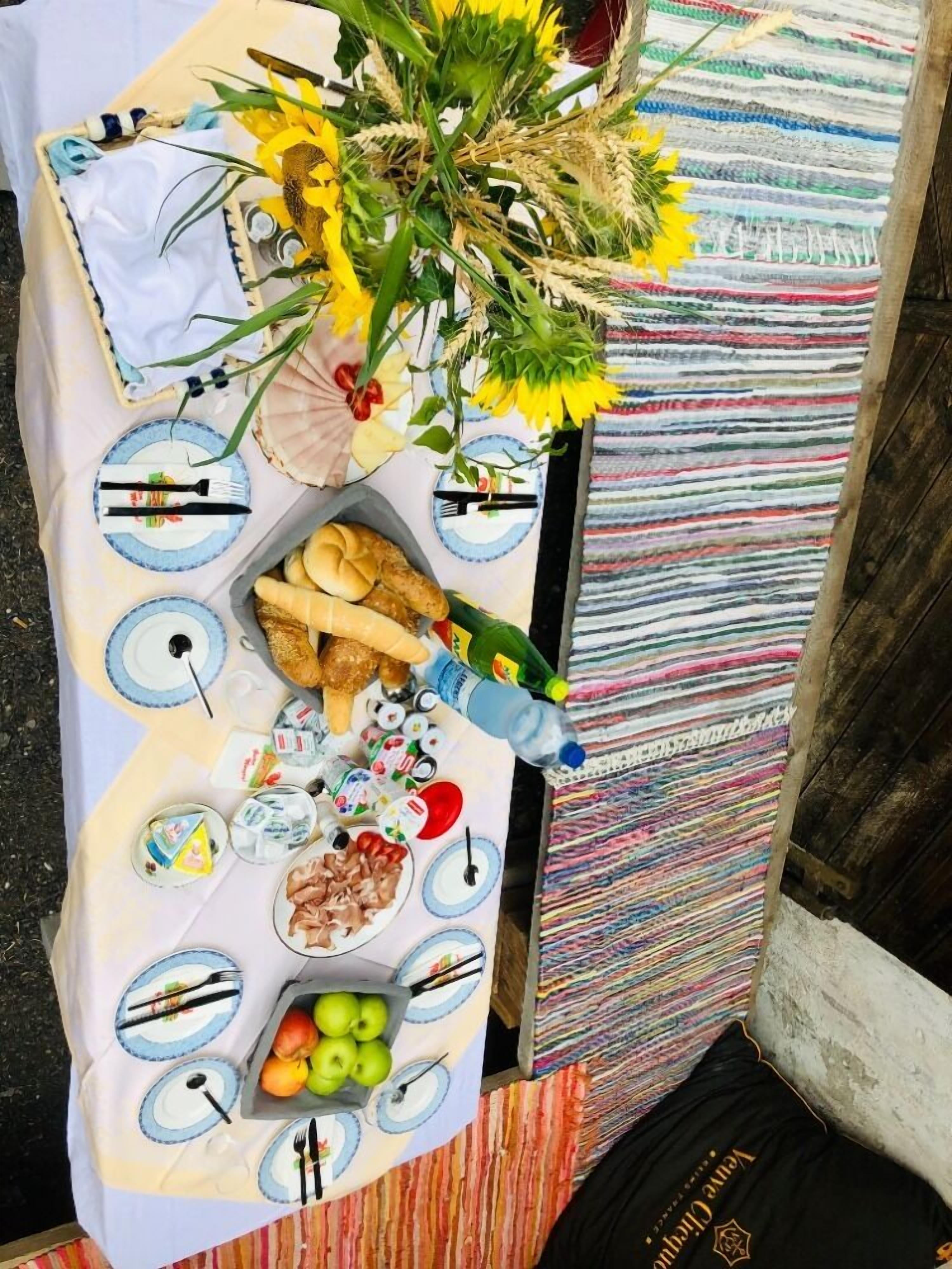 Mesa posta com pratos, talheres, pão e uma variedade de petiscos e frutas.