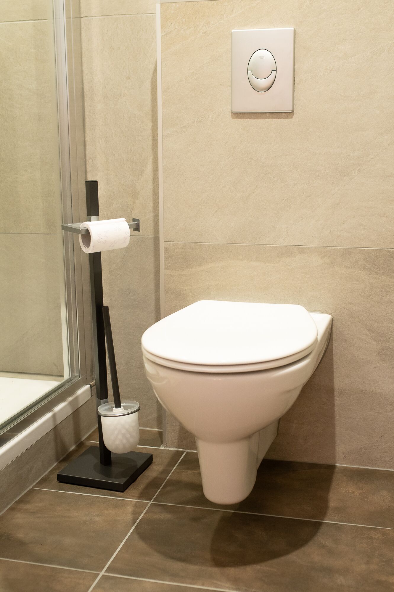 A modern bathroom with a toilet, a toilet paper holder, and a flush button on the wall.