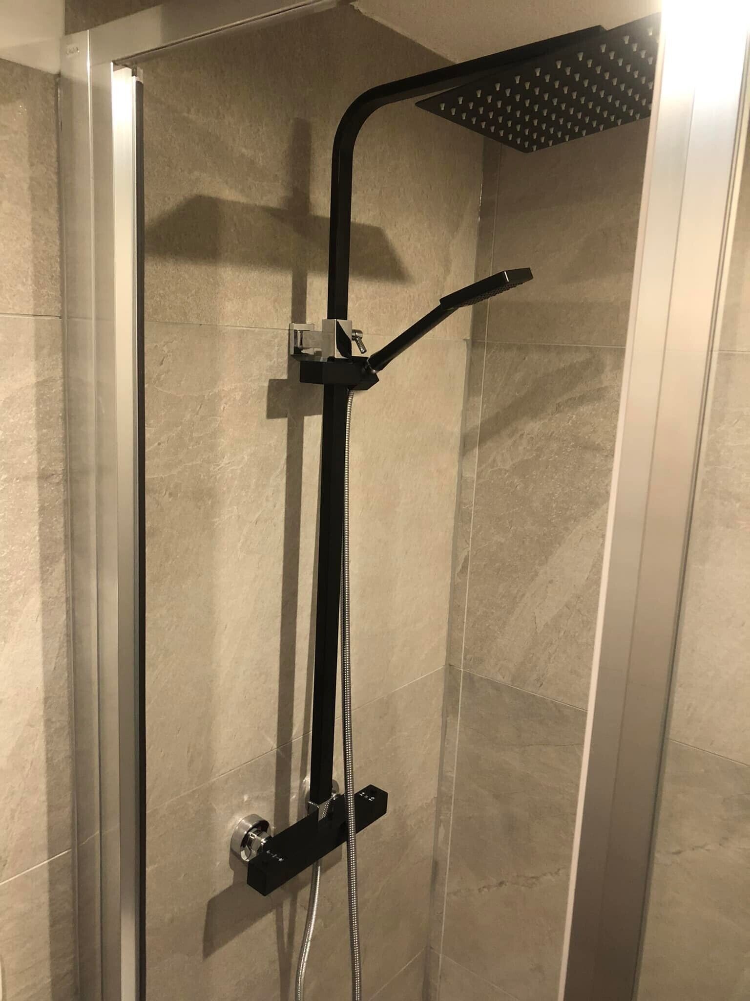 Une douche fermée par des parois en verre, dotée d’un pommeau de douche à main et d’un robinet mural.