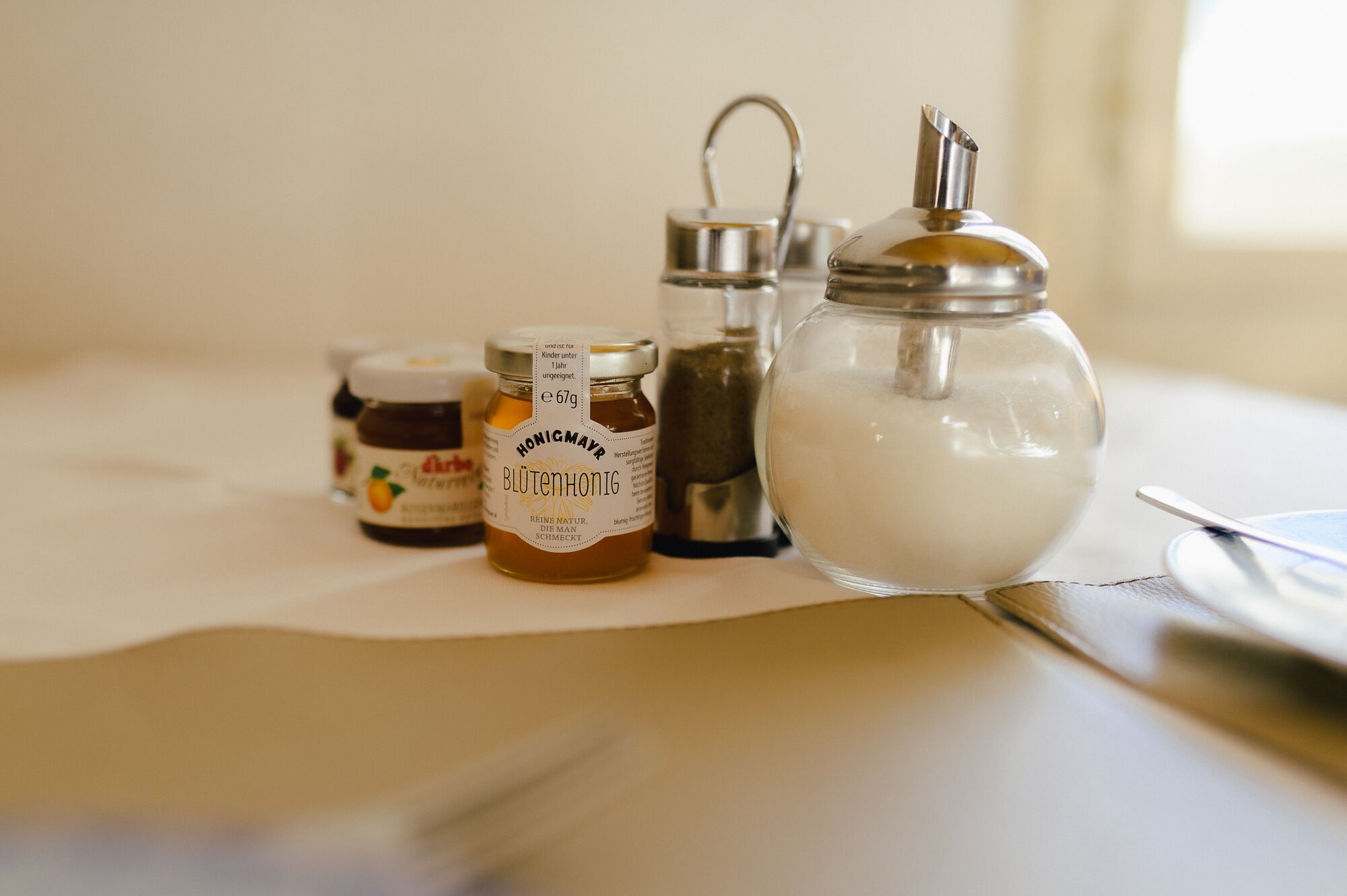 A table with three jars of honey and a sugar bowl.